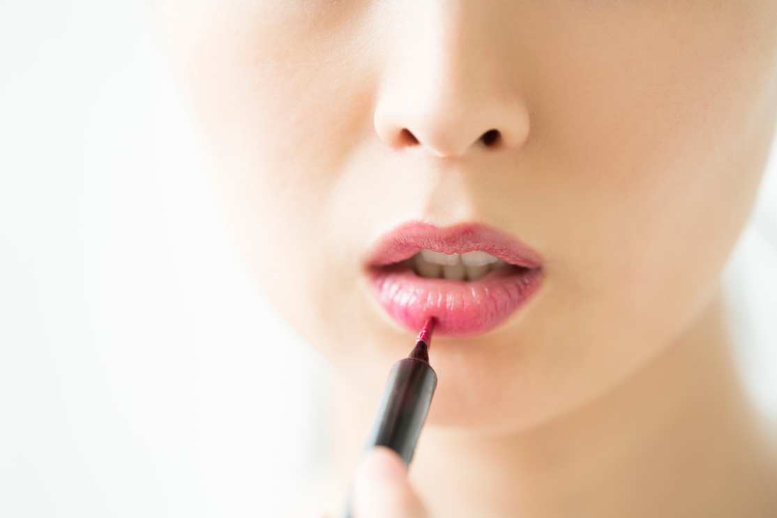 The mouth of a woman making up makeup with a lip liner.